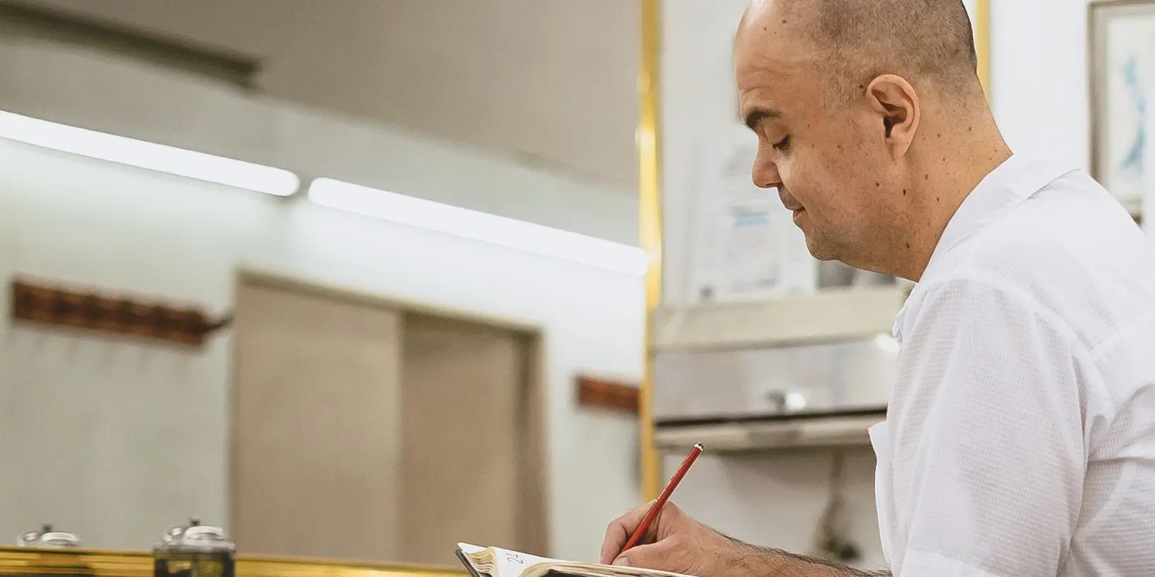A barbershop owner writing quietly in his appointment ledger between clients