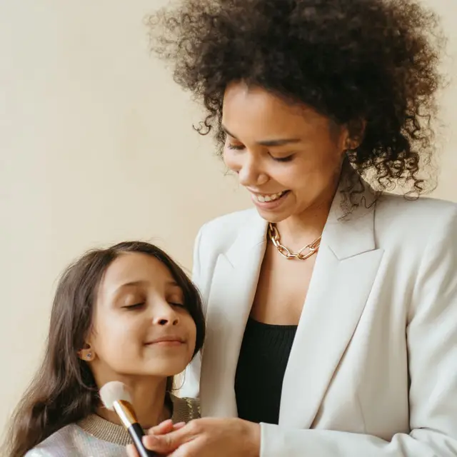 A mother applying makeup to her daughter's cheek