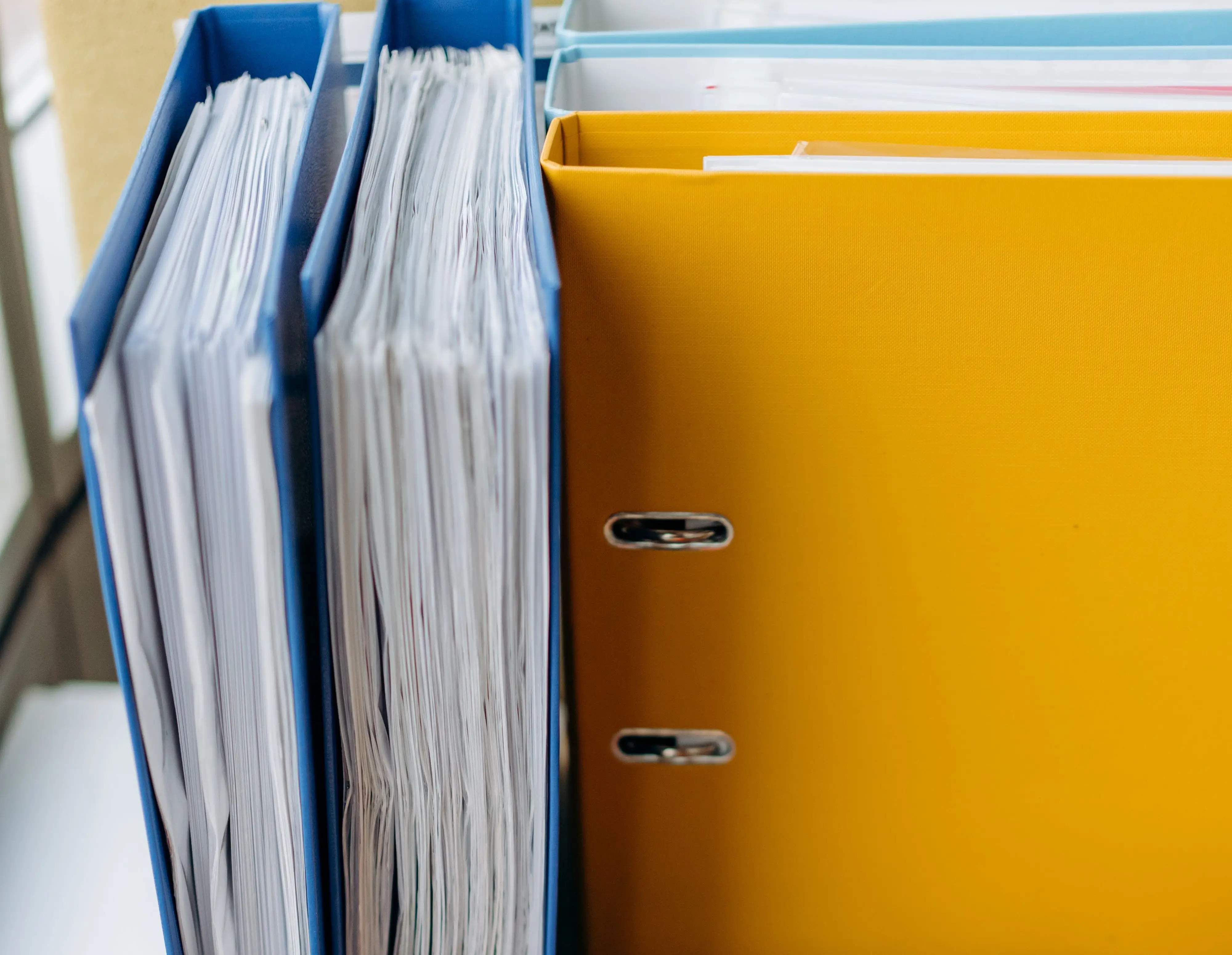 Overstuffed binders and folders piled on a desk, representing a business's disconnected paper systems