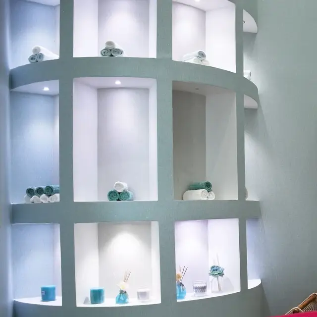 An illuminated boutique spa storage wall with rolled towels, candles, and reed diffusers